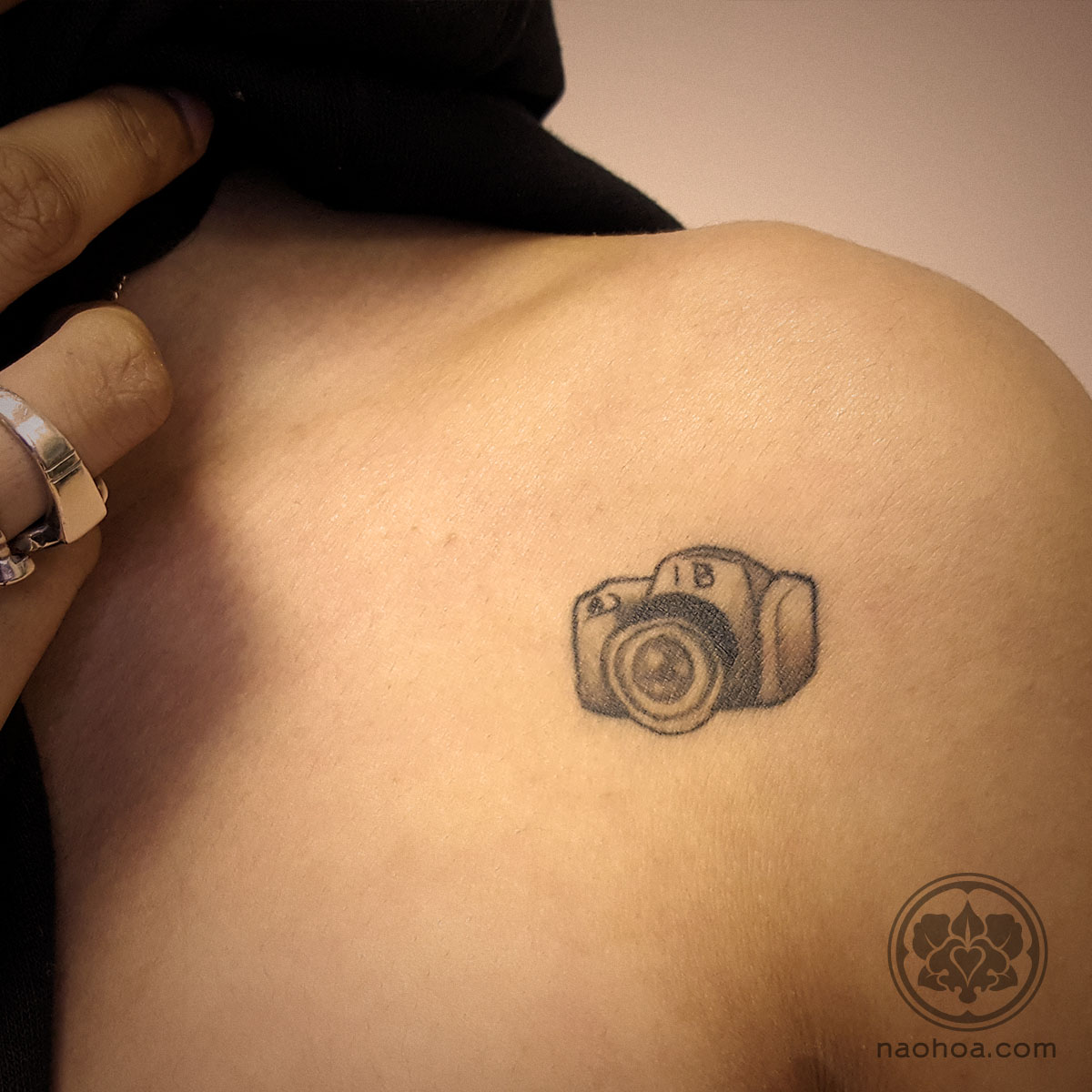 A black and grey tattoo of a small camera, in tribute of the woman's best friend. Designed and tattooed by Naomi Hoang at NAOHOA Luxury Bespoke Tattoos, Cardiff (Wales, UK).