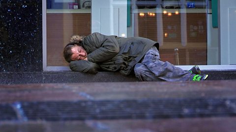 A homeless man sleeping on a pavement.