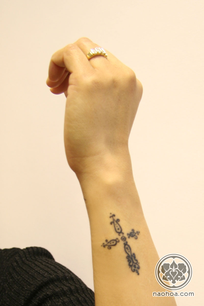 A small, intricate tattoo of a Christian cross on a woman's arm.