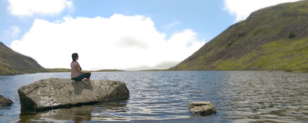 Photograph of Naomi Hoang from NAOHOA Luxury Bespoke Tattoos, Cardiff (Wales, UK) meditating on a rock in the middle of a lake in Snowdonia.