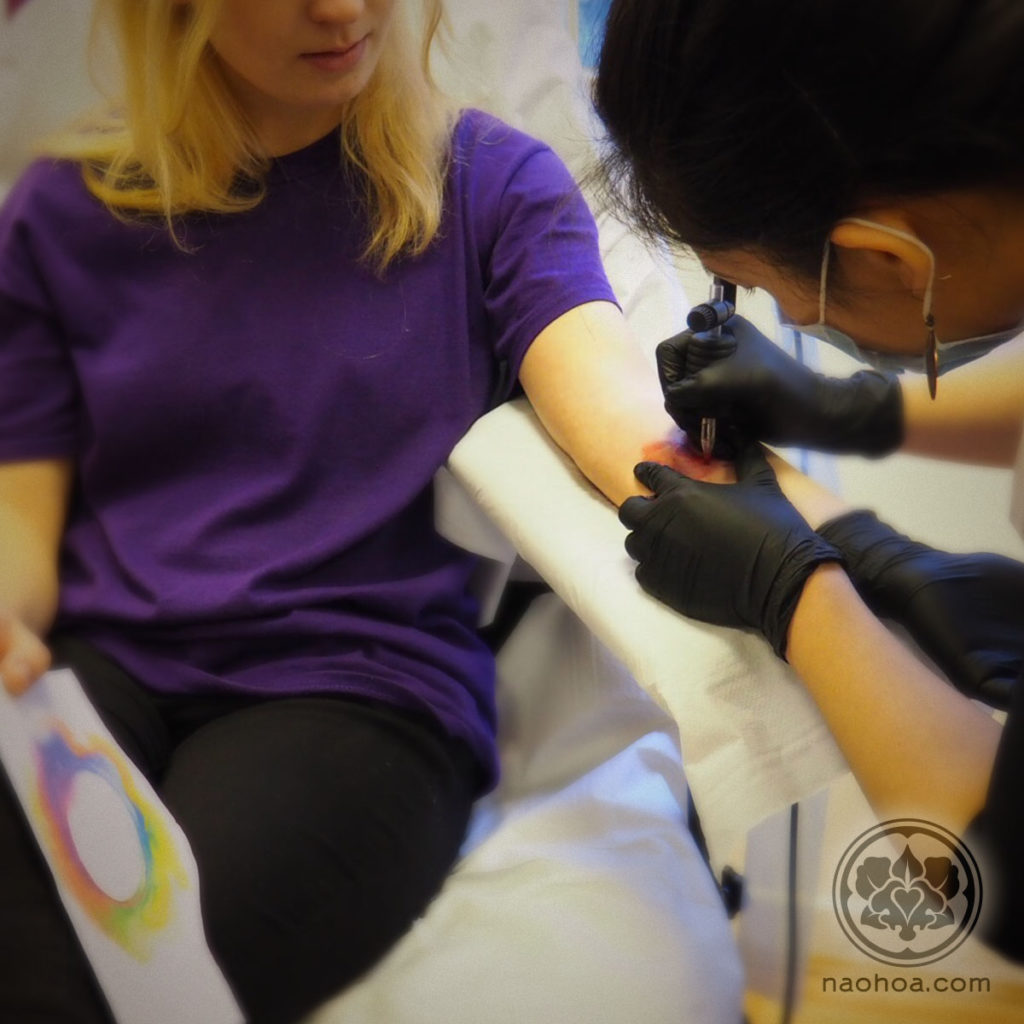 Photo of female tattoo artist Naomi Hoang at work in NAOHOA Luxury Bespoke Tattoos, Cardiff (Wales, UK).